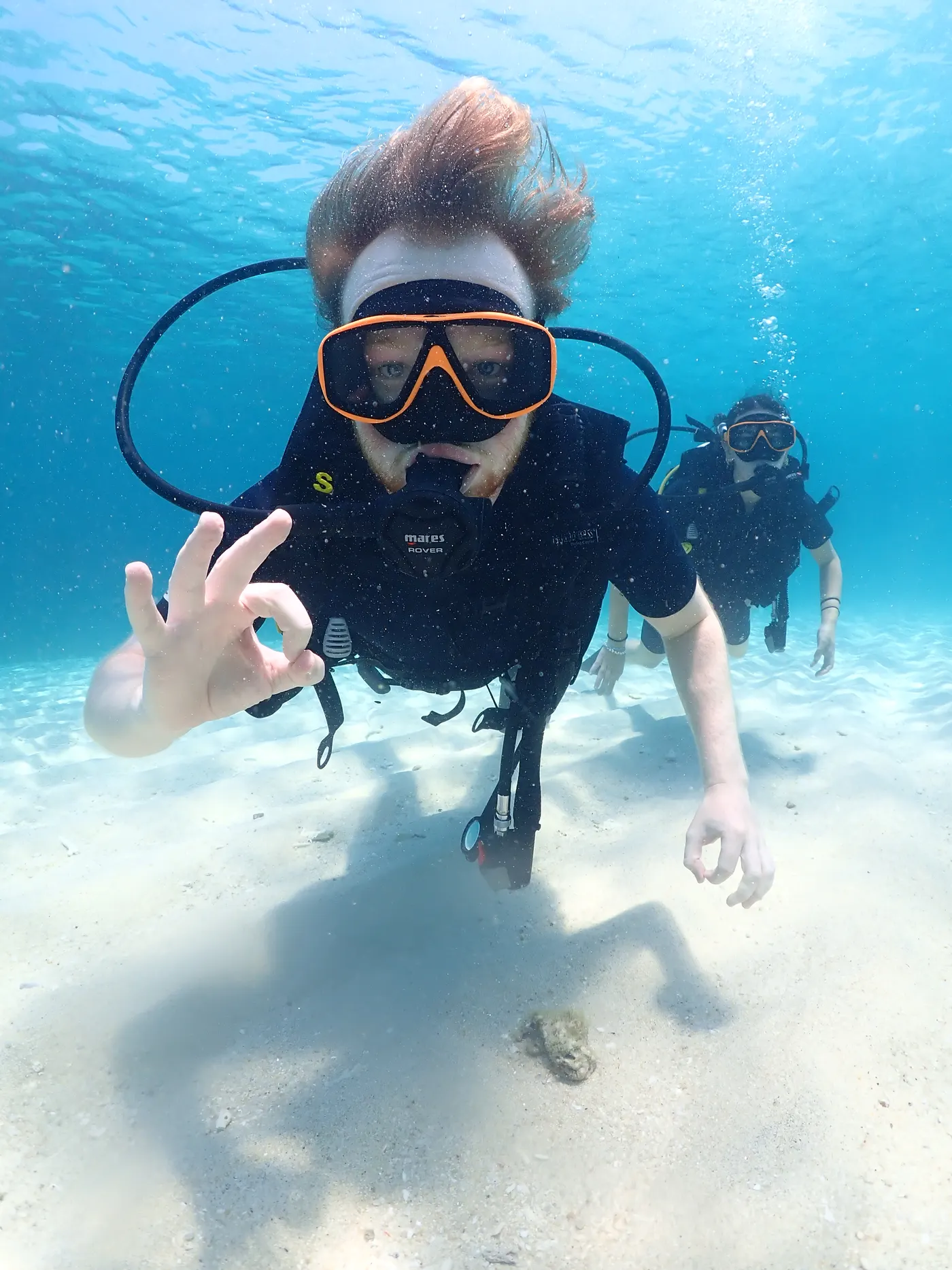 First-time diver giving the OK sign over the sandy bottom with an instructor close behind