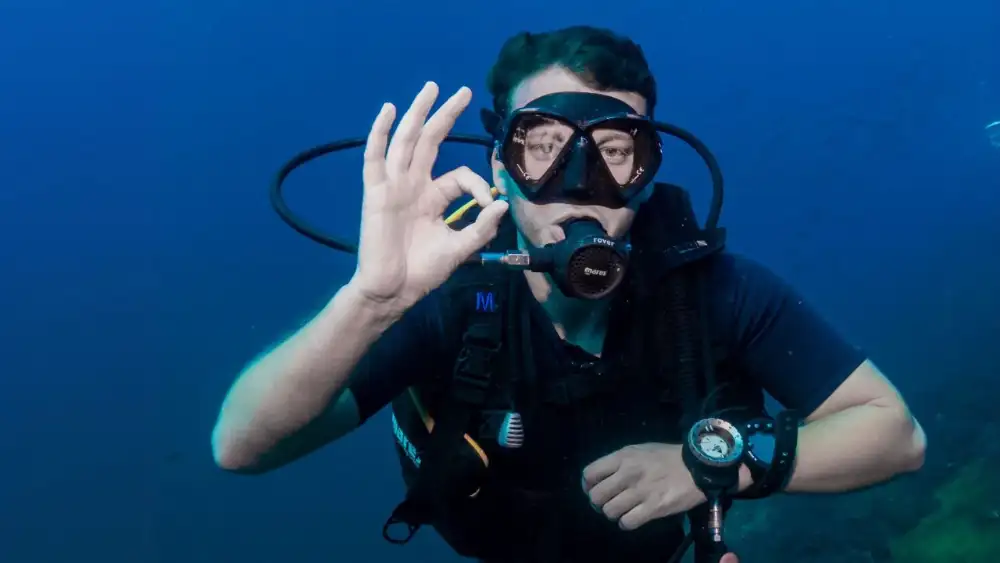 A diver underwater making the OK signal with thumb and index finger forming a circle
