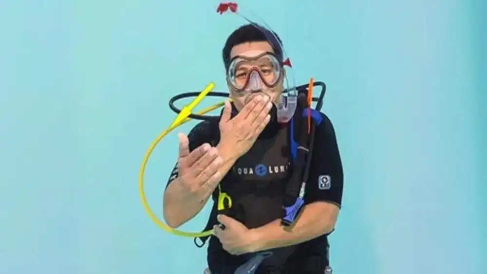 A diver underwater moving a hand back and forth to the mouth to signal share air