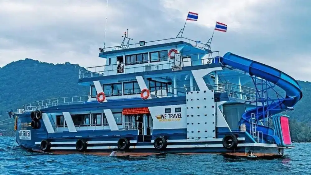 Snorkellers in the water beside a tour boat in a sheltered Koh Tao bay, with the island's green hills in the background