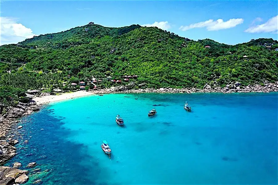 Aow Leuk bay on Koh Tao's east coast, with clear shallow water over reef and sand and boulders along the shore