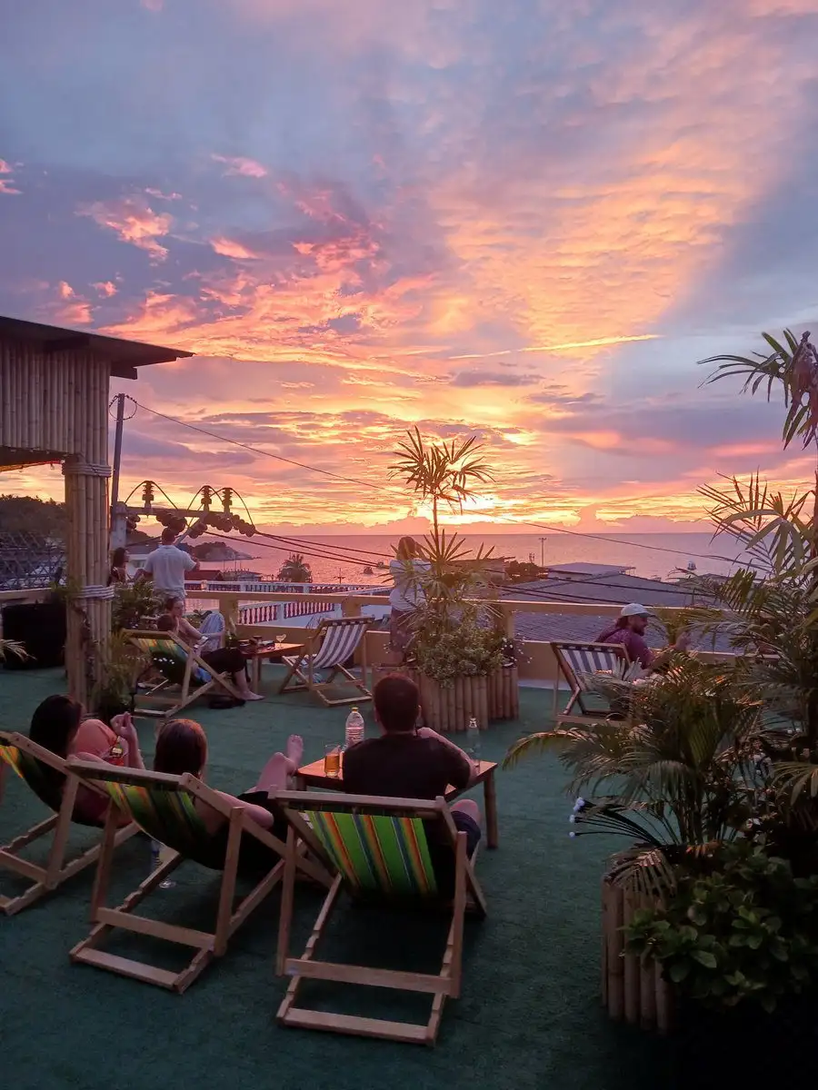 Guests relaxing in deckchairs on the Serve Chilled rooftop garden as a pink and orange sunset lights up the sky over the sea