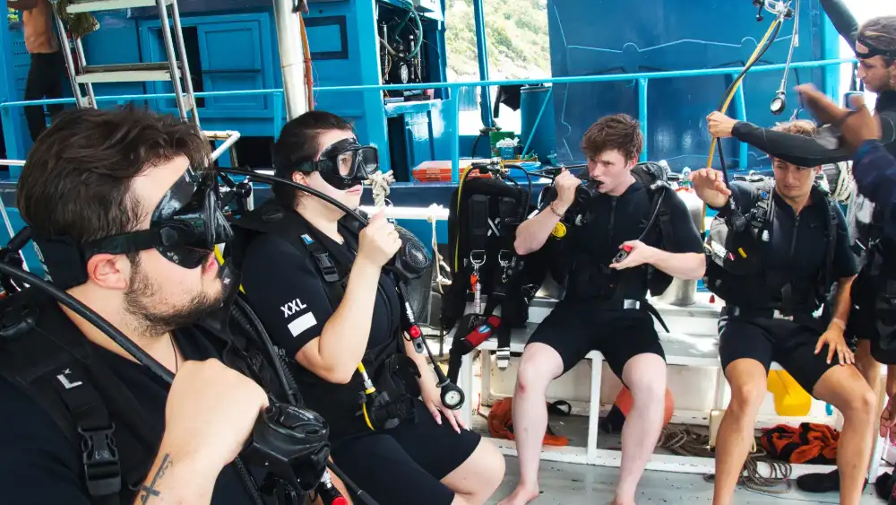 A snorkeller floating at the surface above a scuba diver exploring the reef below in clear tropical water