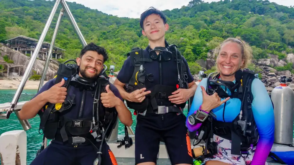 A female divemaster leading a group of divers along a reef off Koh Tao