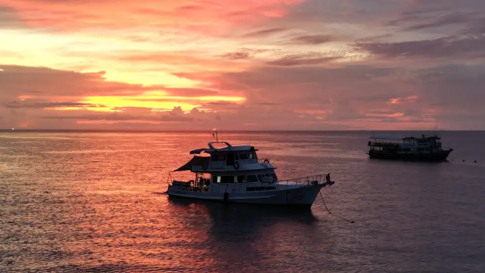 Two dive boats moored off Koh Tao under a vivid orange and pink sunset sky, the calm sea reflecting the colours
