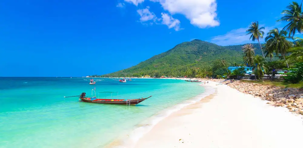 Aerial view of the Koh Phangan coastline with a beach, palm trees and turquoise water