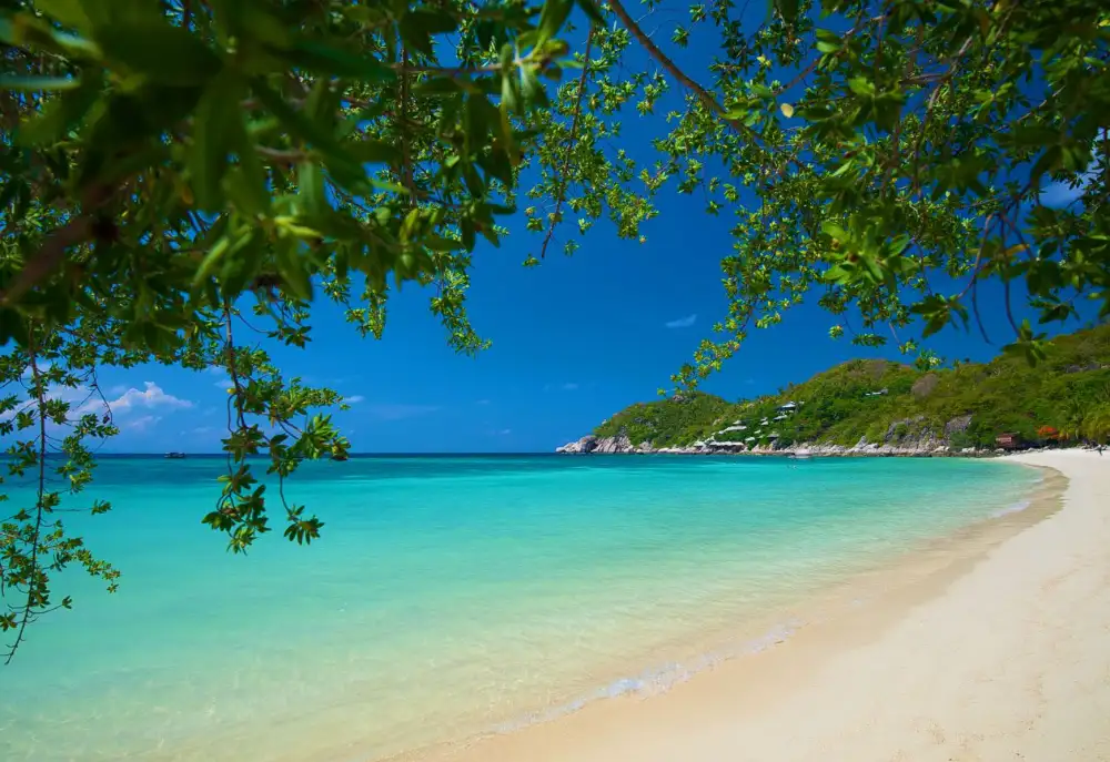 A quiet sandy beach and bay on Koh Tao with clear turquoise water and longtail boats