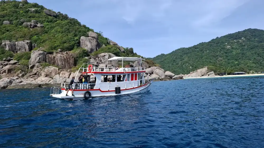 Koh Tao island seen from the sea, green hills above a bay with boats moored in turquoise water