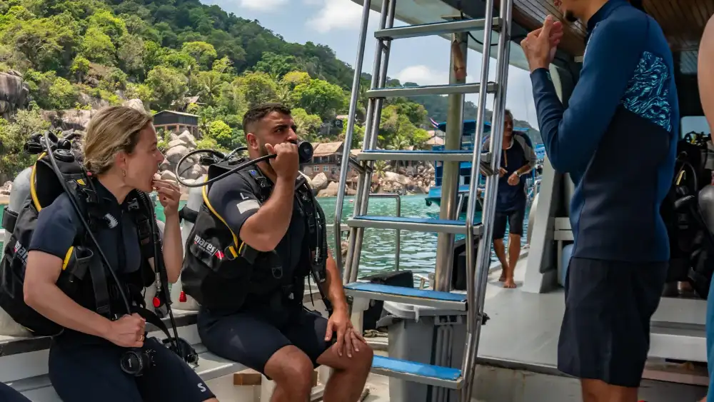 A La Bombona Diving instructor on the dive boat guiding a diver through gear setup before the dive
