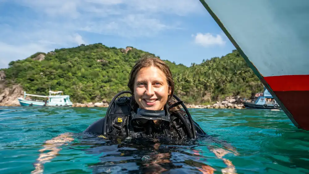 A solo traveller looking out over the turquoise water and green hills of Koh Tao from a viewpoint