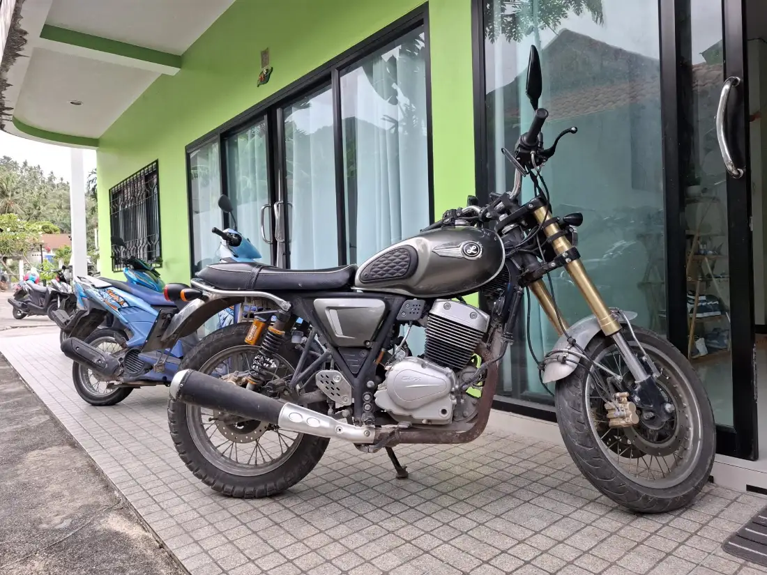 A rental manual motorcycle and scooters parked in front of a green-walled rental shop on Koh Tao