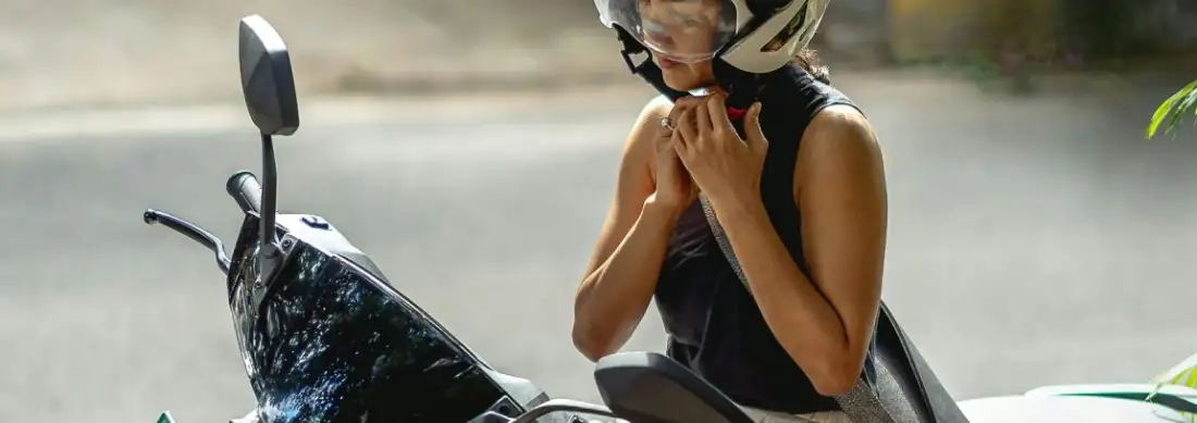 A woman fastening her helmet strap while sitting on a scooter on a Koh Tao road